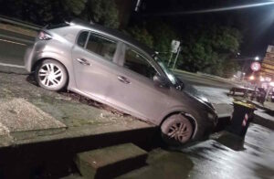 Auto in bilico a Stagno tra il manto stradale e il marciapiede sottostante