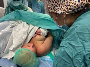 Anche all’ospedale di Livorno, il contatto pelle a pelle è possibile nelle due ore successive al parto cesareo, proprio come avviene per il parto vaginale. I primi a sperimentare questa pratica sono stati mamma Rachele e il piccolo Filippo, nato ieri mattina, 10 febbraio, con taglio cesareo, seguito immediatamente dal contatto diretto con la madre.   Il contatto pelle a pelle consiste in un legame immediato, continuo e sicuro tra madre e neonato, essenziale non solo per favorire l’allattamento, ma anche per stimolare i meccanismi fisiologici del bambino e rafforzare il legame affettivo tra genitori e figlio. Questo processo, che coinvolge aspetti fisici, ormonali ed emotivi, rappresenta la base per una relazione madre-bambino solida e duratura.    “La prima ora di vita extra-uterina è un momento fondamentale in cui il neonato incontra la madre e l’altro genitore, creando il nucleo familiare” spiega Marzia Chellini, ostetrica del dipartimento Materno infantile dell’ASL Toscana nord ovest. “In questo breve lasso di tempo si verifica una sorta di imprinting reciproco: il bambino riconosce la madre e il partner, attivando i suoi istinti naturali, mentre la madre è pronta ad accoglierlo.”   Il piccolo Filippo, figlio di Rachele e Matteo, entrambi residenti a Piombino, è stato accolto con grande attenzione dallo staff dell’ospedale di Livorno. Appena nato e dopo il primo vagito, è stato delicatamente adagiato sul petto della mamma sotto la supervisione dell’intera équipe.   Grazie a questa pratica, Filippo ha effettuato la sua prima poppata pochi minuti dopo la nascita. Secondo le linee guida dell’Oms e dell’Unicef, questi momenti sono fondamentali perché favoriscono un migliore adattamento del neonato alla vita extrauterina e, grazie al colostro materno, contribuiscono alla formazione di una flora intestinale ottimale, rafforzando il sistema immunitario e riducendo il rischio di patologie infantili.   L’introduzione del primo parto cesareo “dolce” all’ospedale di Livorno è il risultato di un lungo percorso di preparazione interdisciplinare, che arricchisce ulteriormente l’offerta assistenziale garantendo un’esperienza di nascita all’insegna delle migliori pratiche.   L'equipe che ha seguito il primo parto cesareo "dolce" all'ospedale di Livorno è composta dalle ostetriche Benedetta Del Bimbo, Luca Dini, Elena Chetoni, dall'infermiera Simona Panicucci, dai ginecologi Gianluca Marino e Alba Fissi, dalle anestesiste Chiara Maggini e Maria Luisa Ceraolo, dai pediatri Niccolò Carli e Erika Spada e dal direttore dell'unità di Neonatologie e pediatria di Livorno Roberto Danieli. 